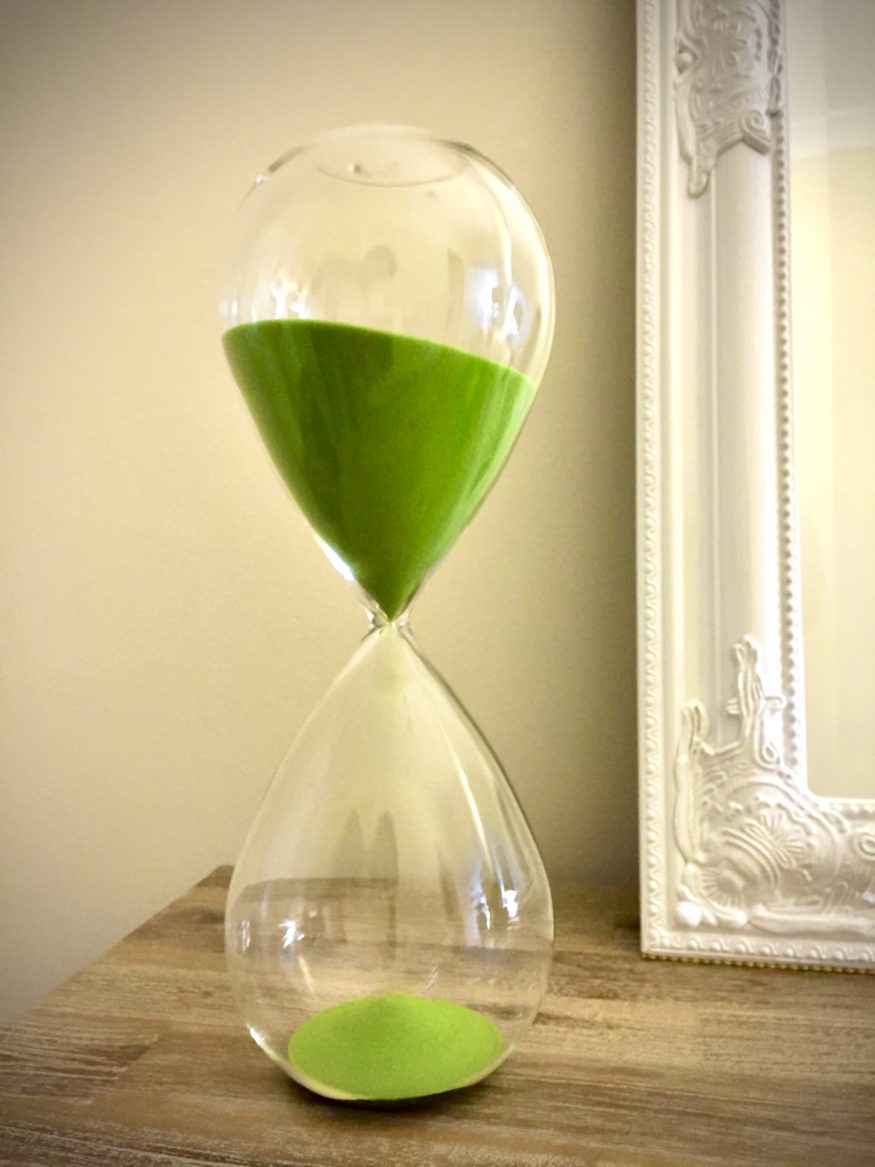 Home hourglass with green sand in front of a mirror